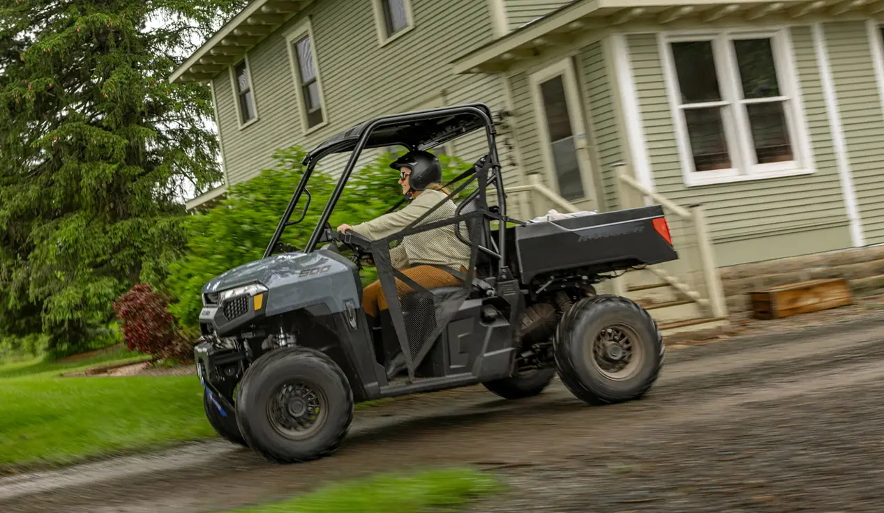 A person driving through their yard in a Polaris RANGER 500 UTV.