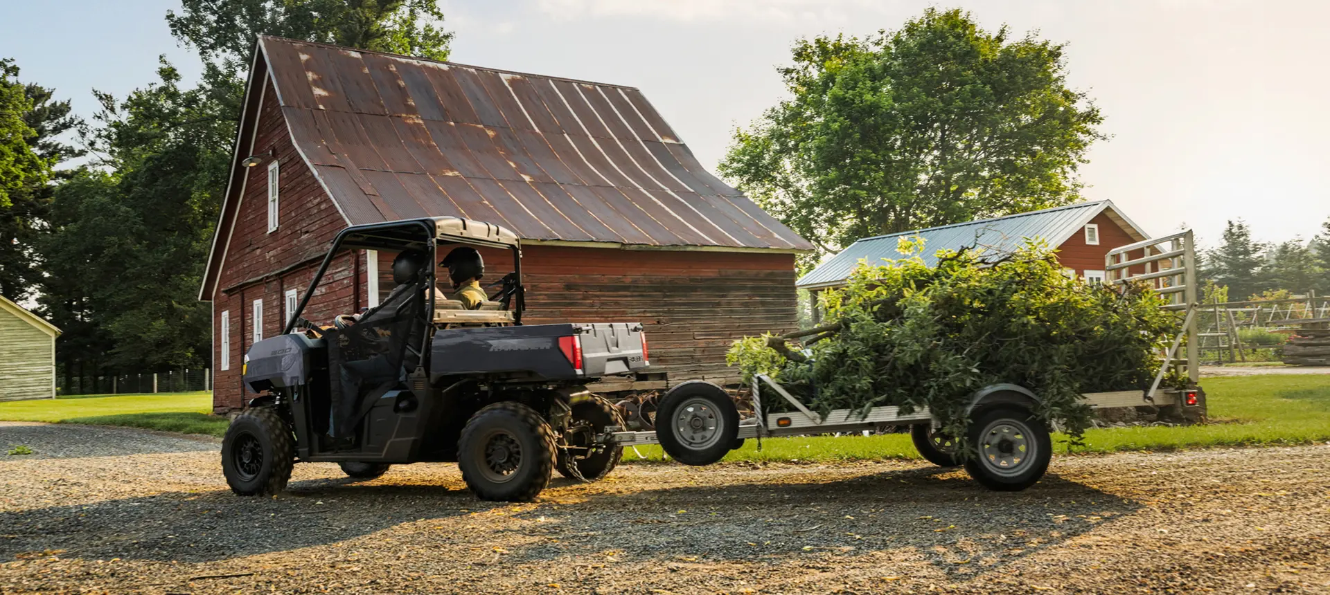 2 riders in a Polaris RANGER 500 UTV pulling a trailer loaded with debris.