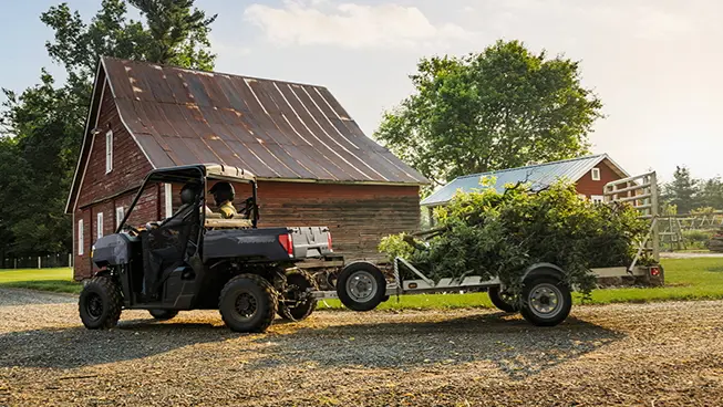 2 riders in a Polaris RANGER 500 UTV pulling a trailer loaded with debris.