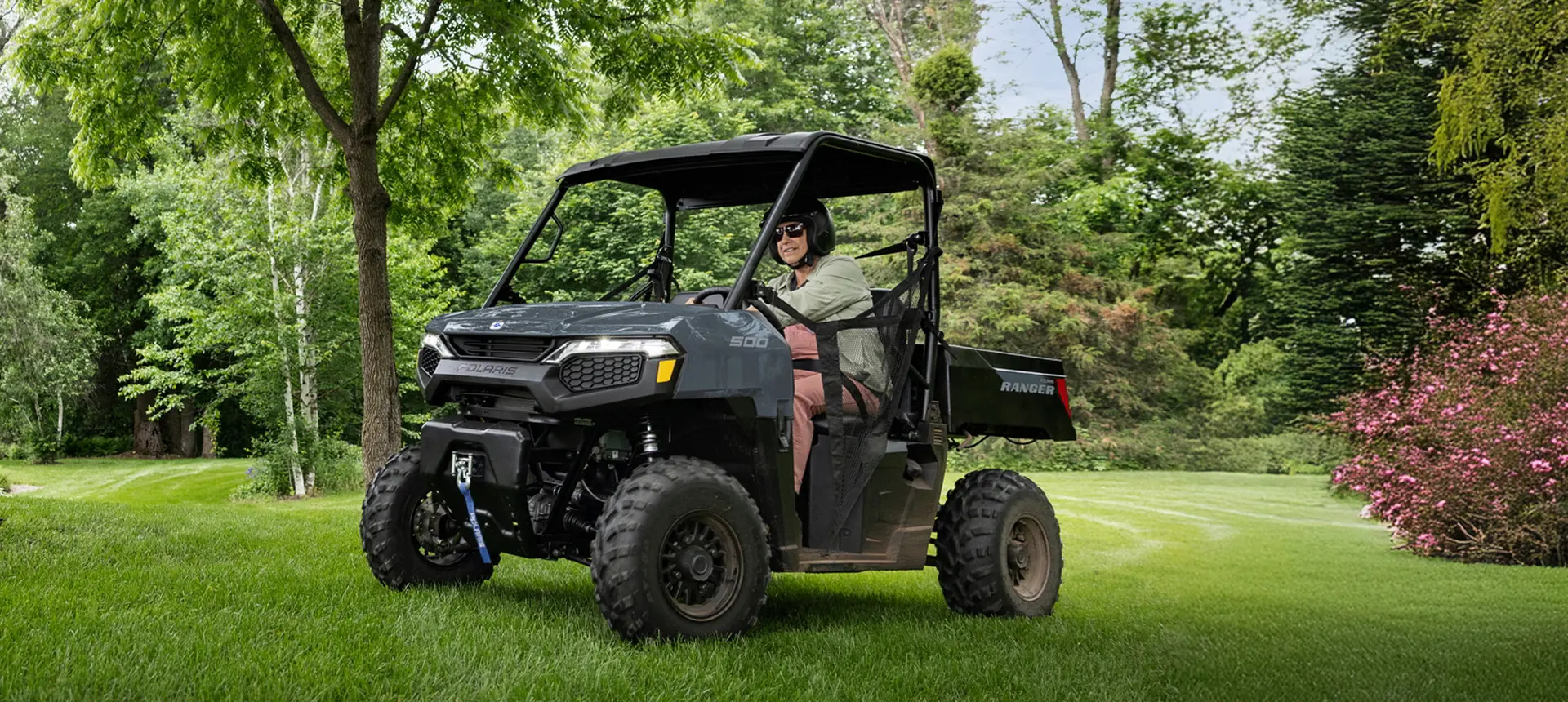 A person driving through their yard in a stealth gray Polaris RANGER 500 UTV.