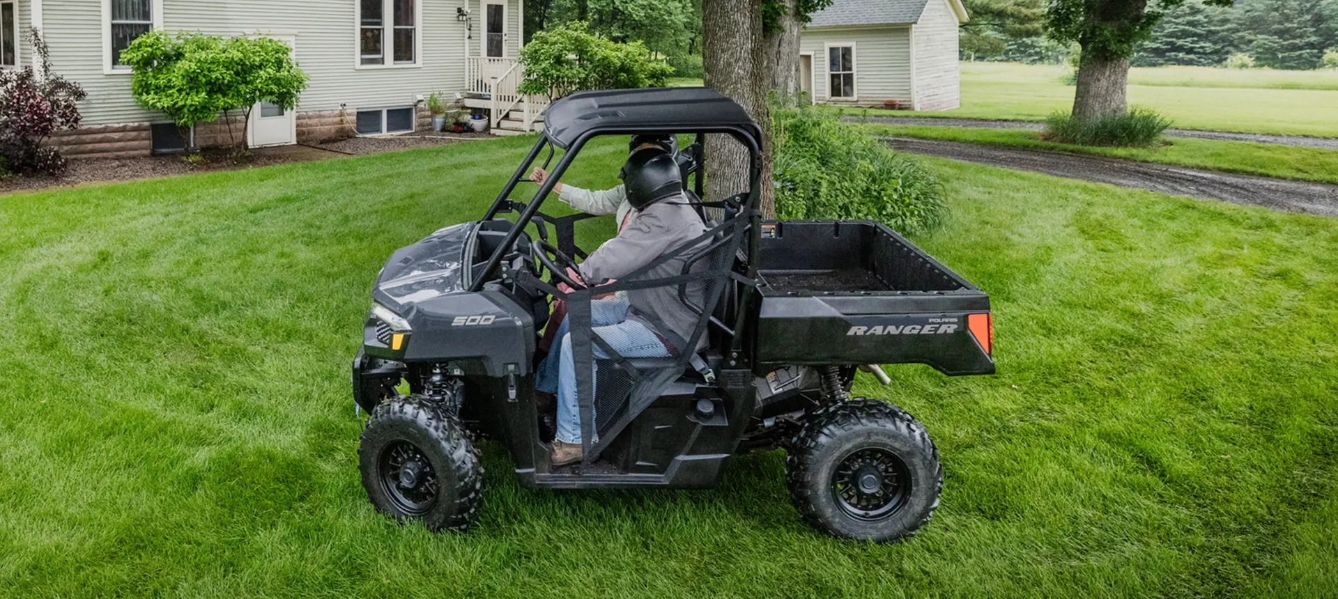 2 riders driving around a tree in a Polaris RANGER 500 utility vehicle.