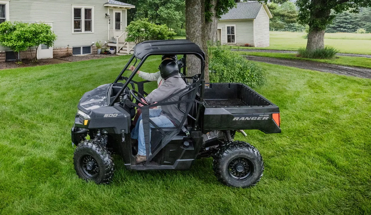 2 riders driving around a tree in a Polaris RANGER 500 utility vehicle.