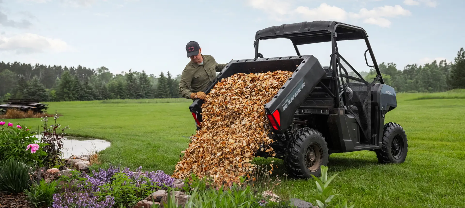 A person unloading leaves from the cargo box of a Polaris RANGER 500 utility vehicle.
