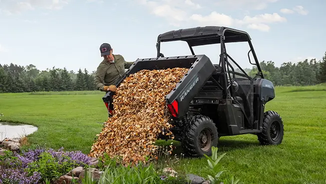 A person unloading leaves from the cargo box of a Polaris RANGER 500 utility vehicle.