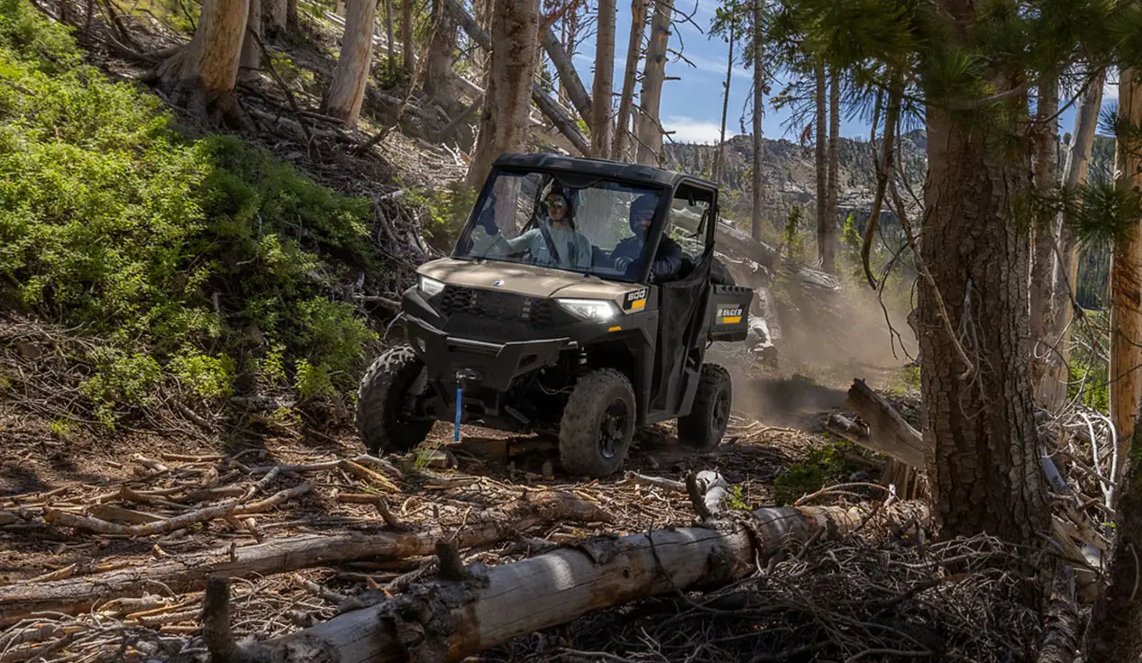 A Polaris RANGER 600 UTV driving over branches in a forest.