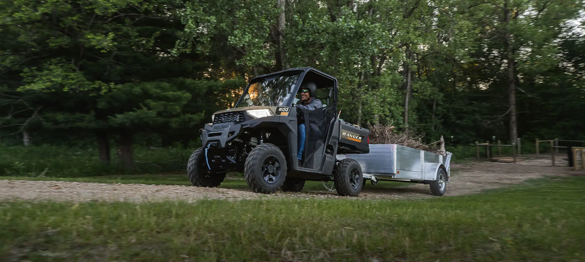 A Polaris RANGER 600 UTV pulling a trailer loaded with debris.