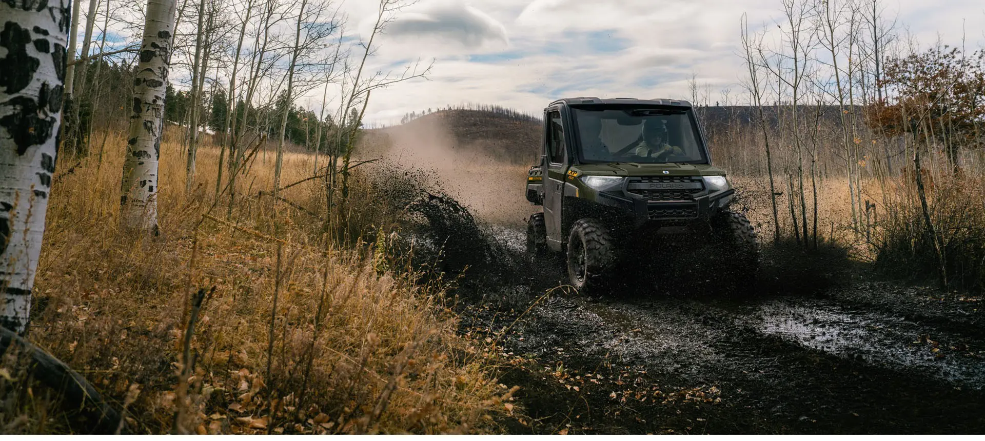 2 riders in a Polaris RANGER XP 1000 NorthStar UTV driving on a muddy trail.
