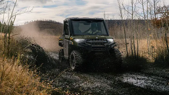 2 riders in a Polaris RANGER XP 1000 NorthStar UTV driving on a muddy trail.