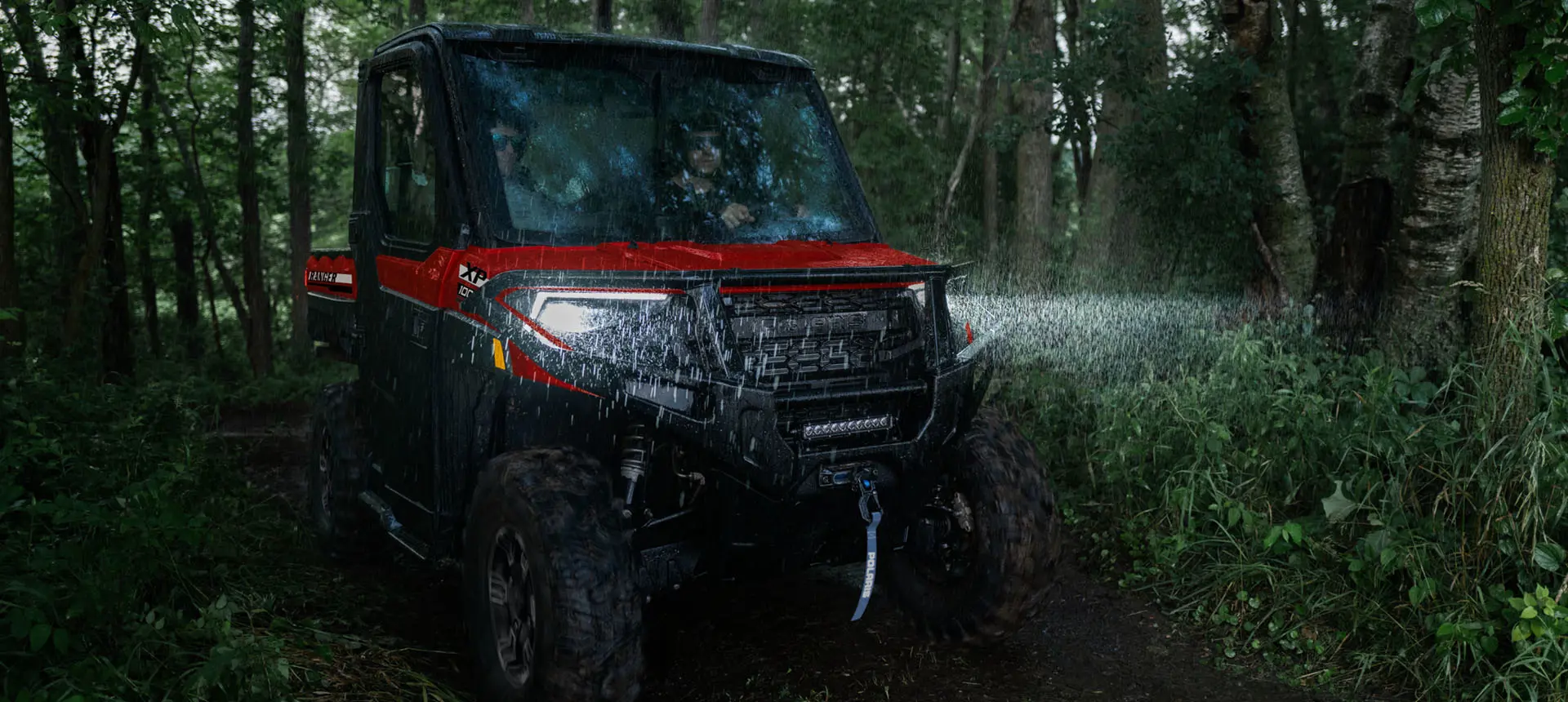 A Polaris RANGER XP 1000 NorthStar UTV with headlights illuminated driving in the forest in the rain.
