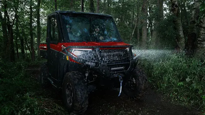A Polaris RANGER XP 1000 NorthStar UTV with headlights illuminated driving in the forest in the rain.