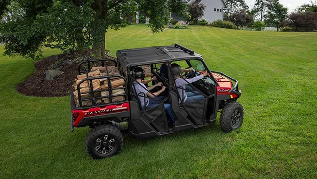 4 riders in a Polaris RANGER CREW XP 1000 UTV hauling wood in the cargo box.