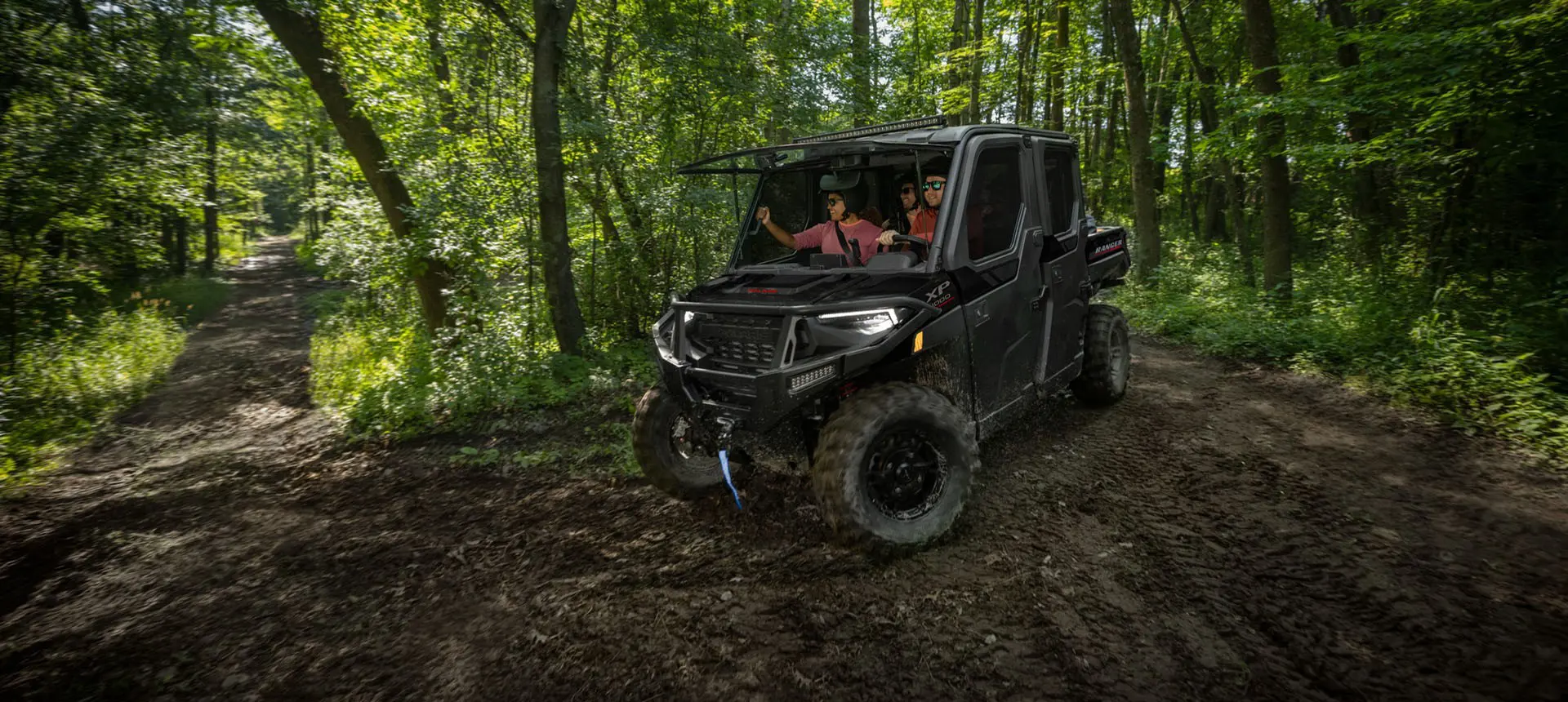 4 riders in a Polaris RANGER XP 1000 NorthStar Trail Boss Edition UTV with the windshield tipped out in the forest.