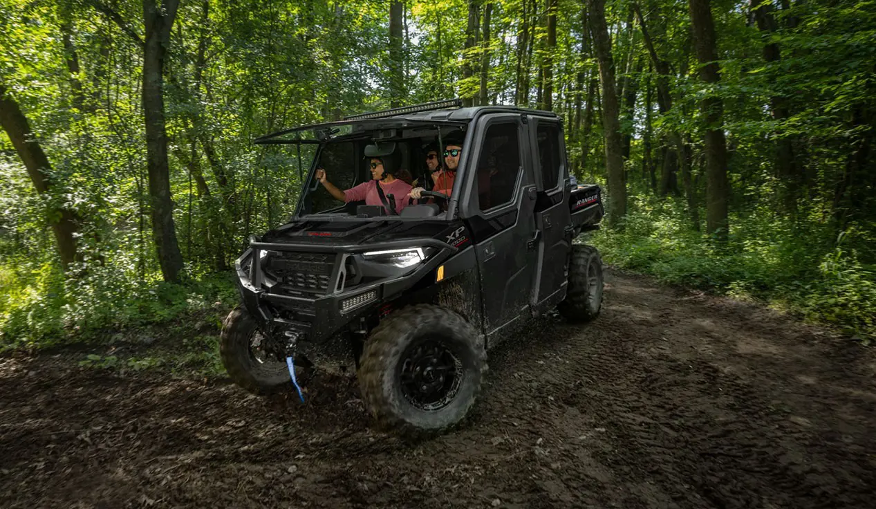 4 riders in a Polaris RANGER XP 1000 NorthStar Trail Boss Edition UTV with the windshield tipped out in the forest.