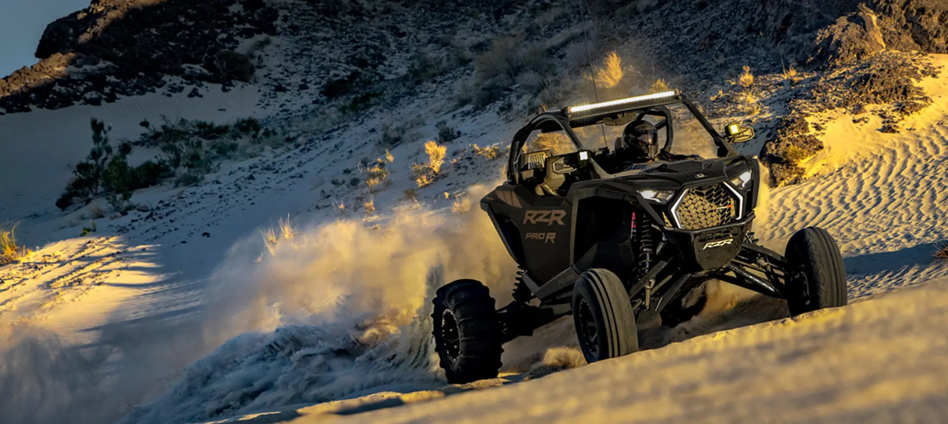 A Matte Super Graphite Polaris RZR Pro R side-by-side driving up hill in the desert.
