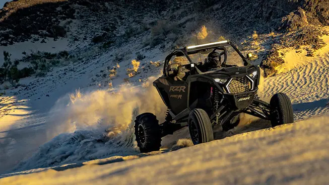 A Matte Super Graphite Polaris RZR Pro R side-by-side driving up hill in the desert.