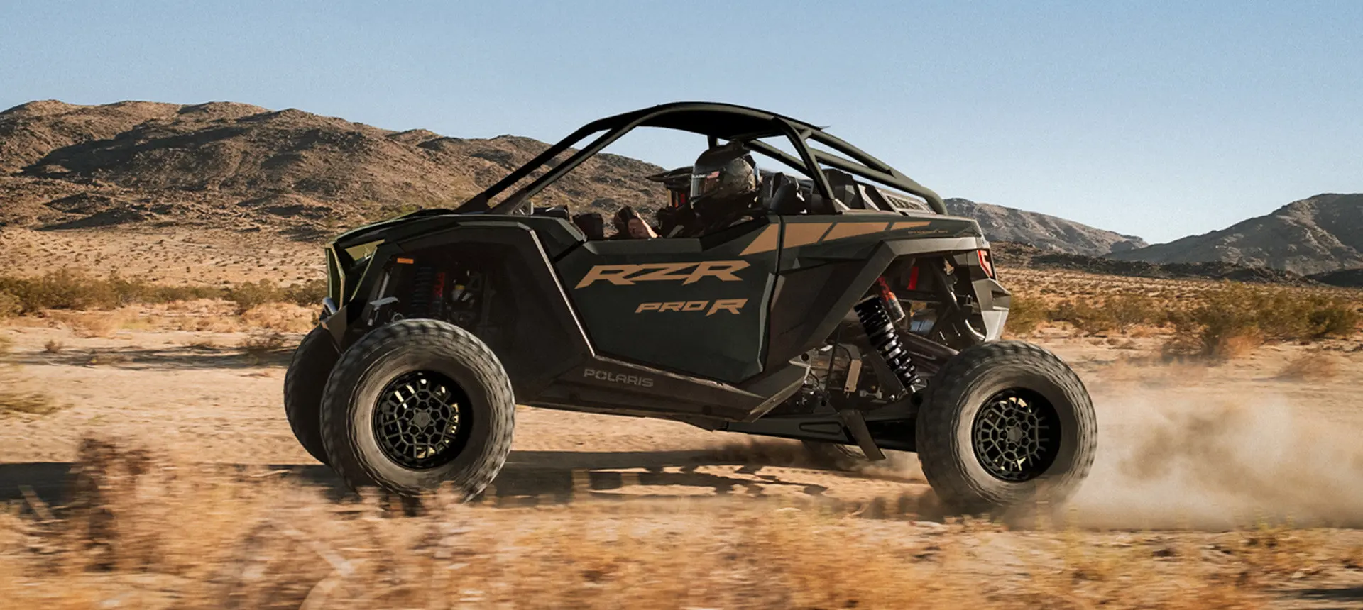 Side profile of a Polaris RZR Pro R side-by-side throwing sand in the dunes.