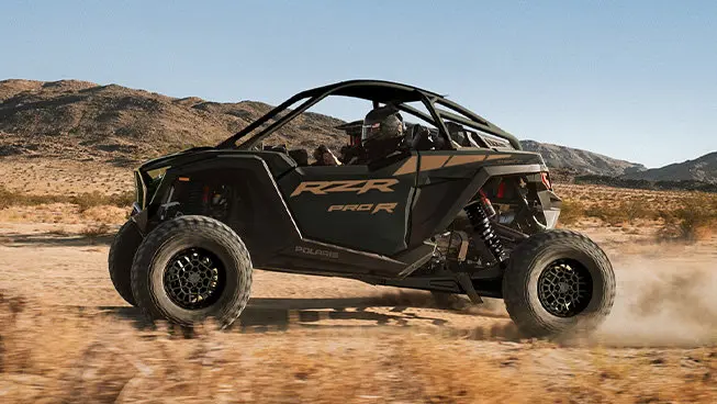 Side profile of a Polaris RZR Pro R side-by-side throwing sand in the dunes.