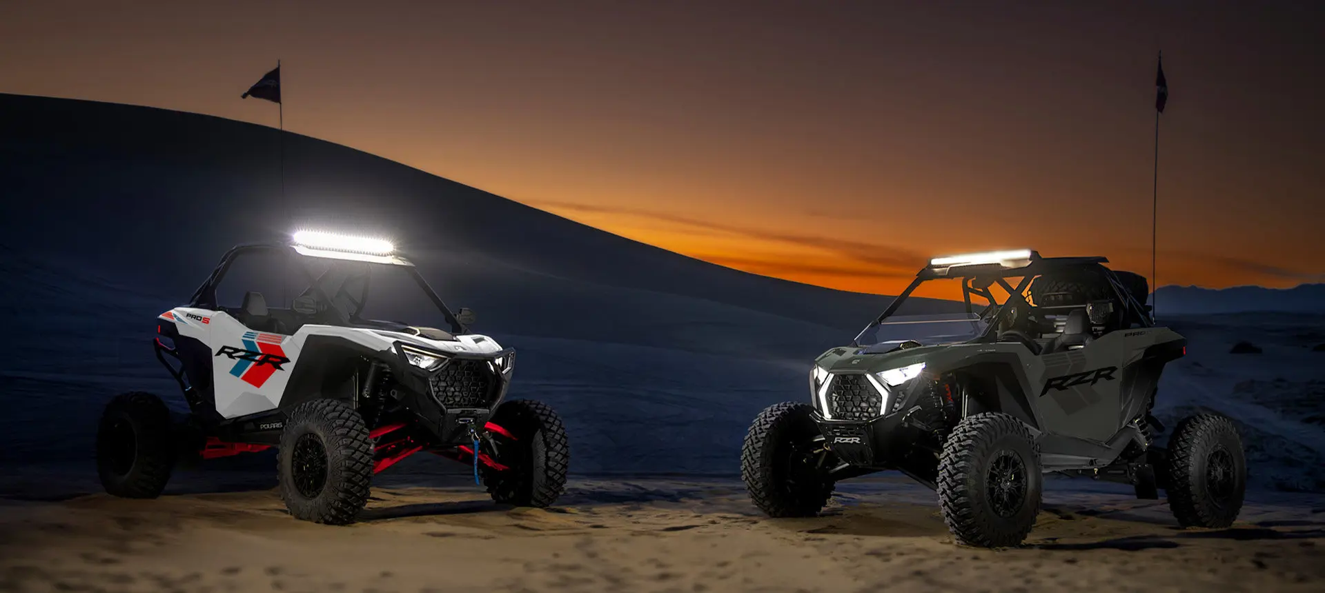 2 Polaris RZR Pro S side-by-sides with headlights illuminated.
