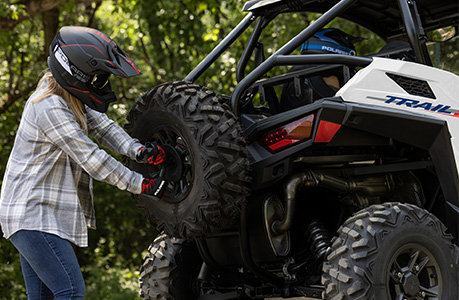 A person grabbing the spare tire from the rear end of Polaris RZR Trail side-by-side while in the forest.