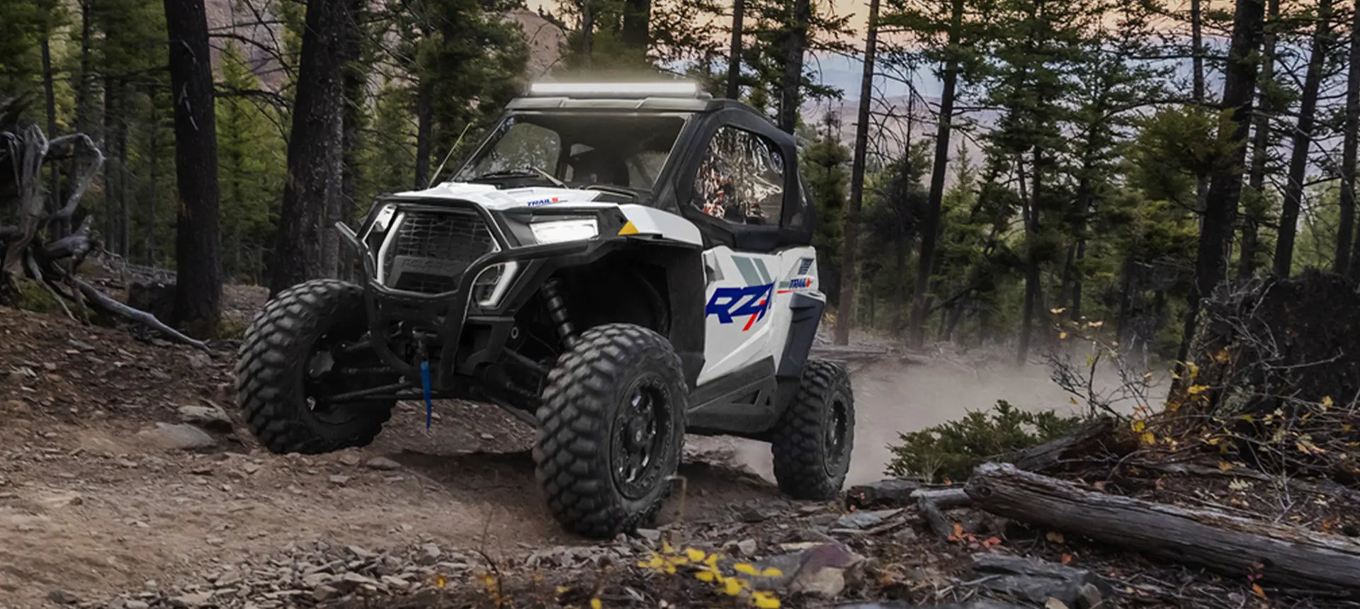 A person in a Polaris RZR Trail side-by-side driving down a forest trail.
