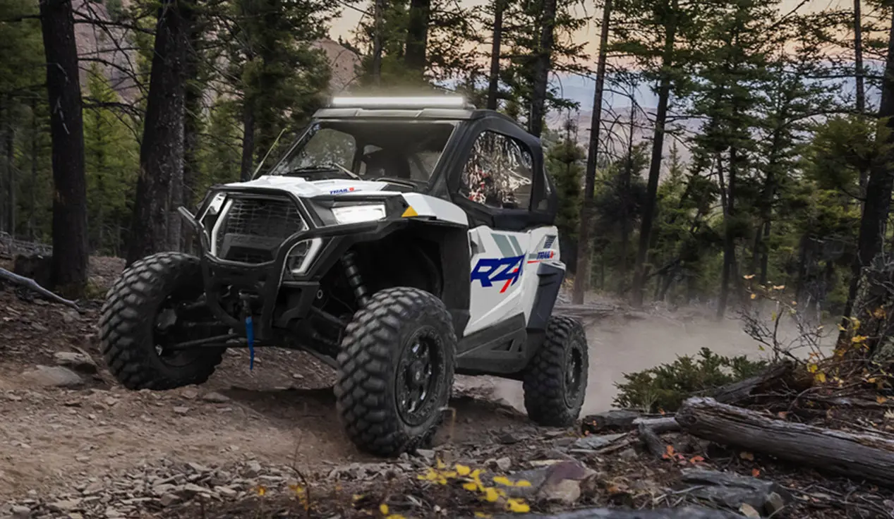 A person in a Polaris RZR Trail side-by-side driving down a forest trail.