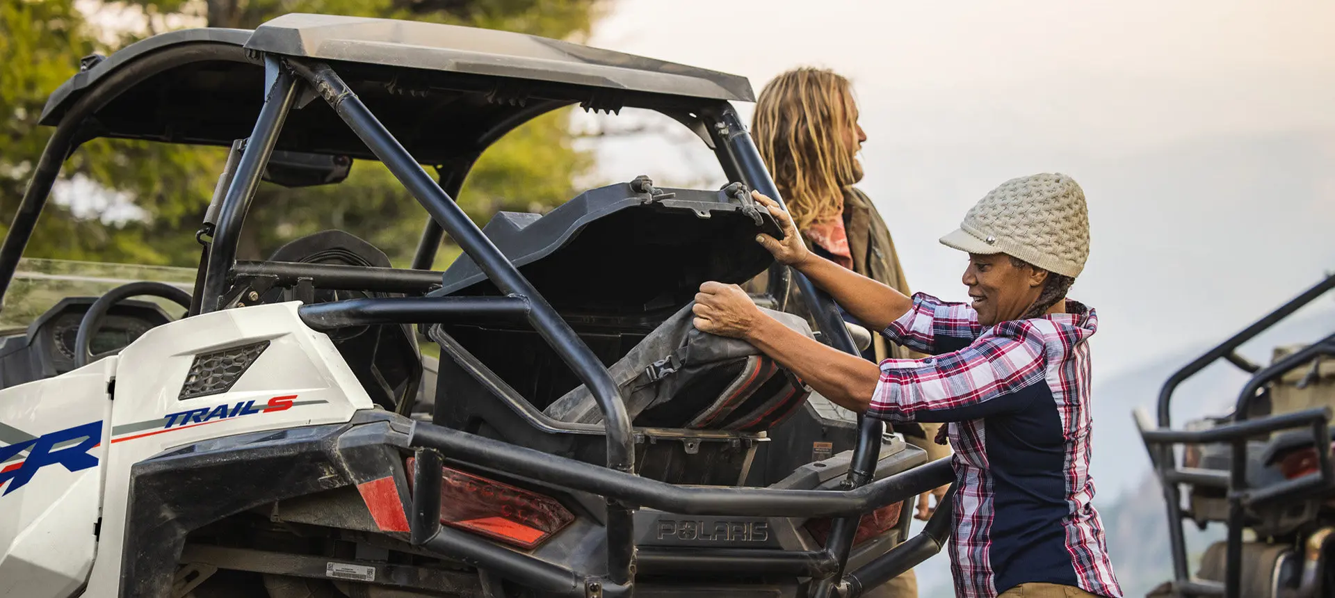 A person grabbing gear from the cargo area of a Polaris RZR Trail side-by-side.