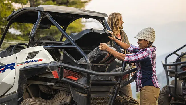 A person grabbing gear from the cargo area of a Polaris RZR Trail side-by-side.