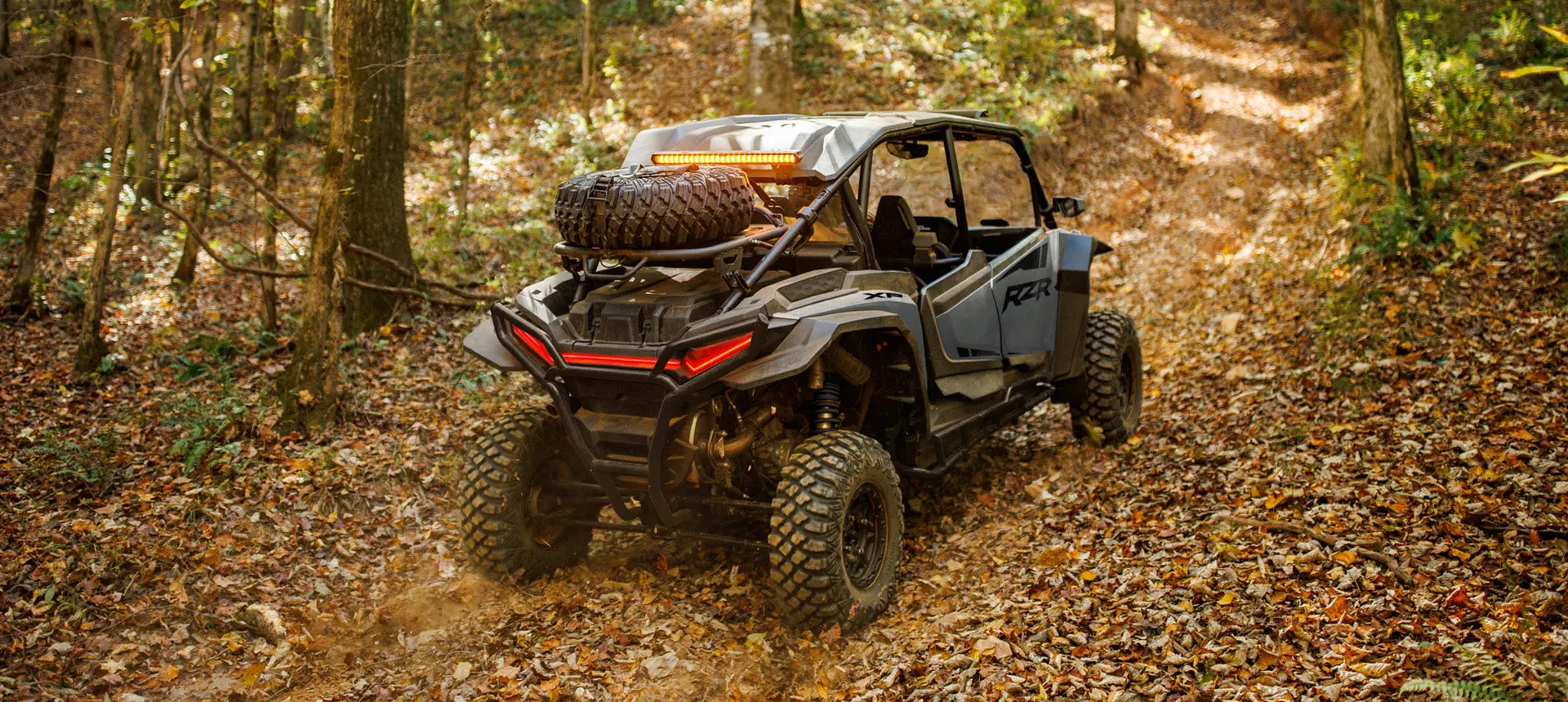 Rear view of a Polaris RZR XP 4 side-by-side cruising on a trail with a spare tire carrier installed.