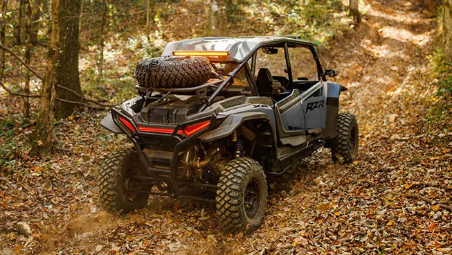 Rear view of a Polaris RZR XP 4 side-by-side cruising on a trail with a spare tire carrier installed.