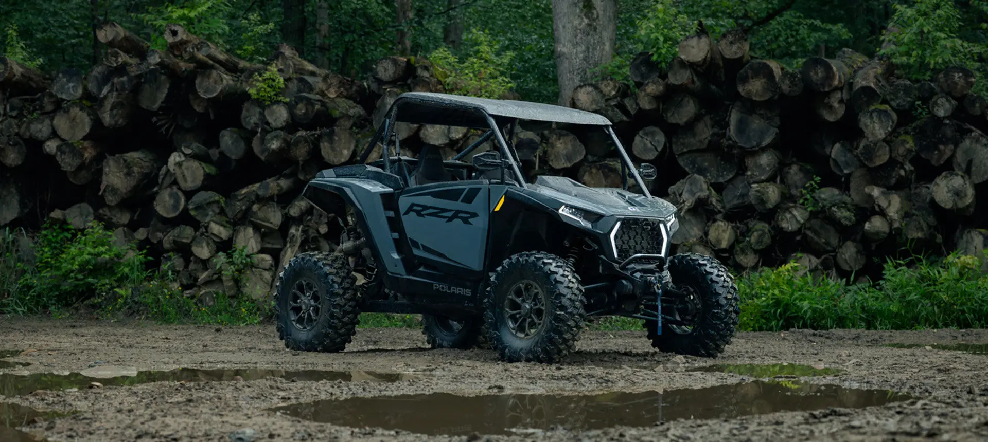 Polaris RZR XP S side-by-side parked near a pile of logs in the forest.