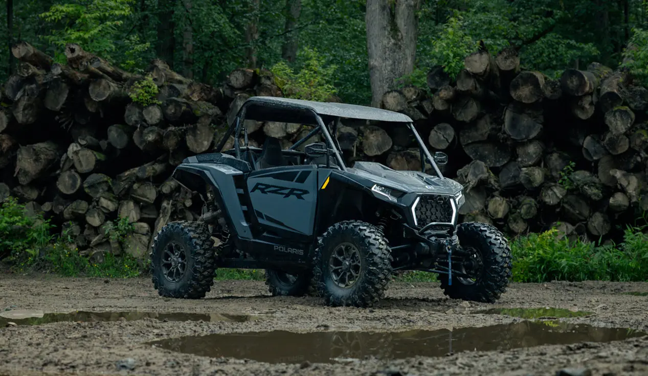 Polaris RZR XP S side-by-side parked near a pile of logs in the forest.
