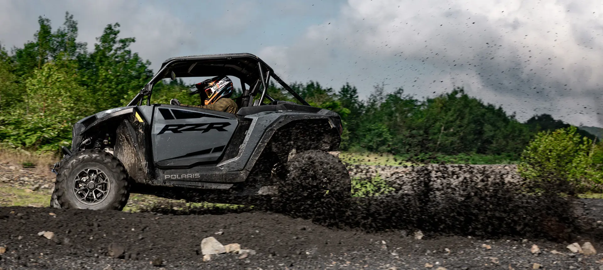 Side profile of a RZR XP side-by-side driving through the mud.