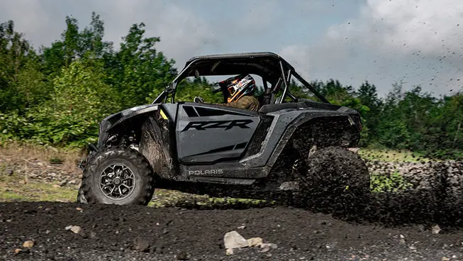 Side profile of a RZR XP side-by-side driving through the mud.