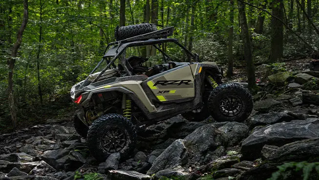 Side profile of a RZR XP side-by-side climbing over rocky terrain.