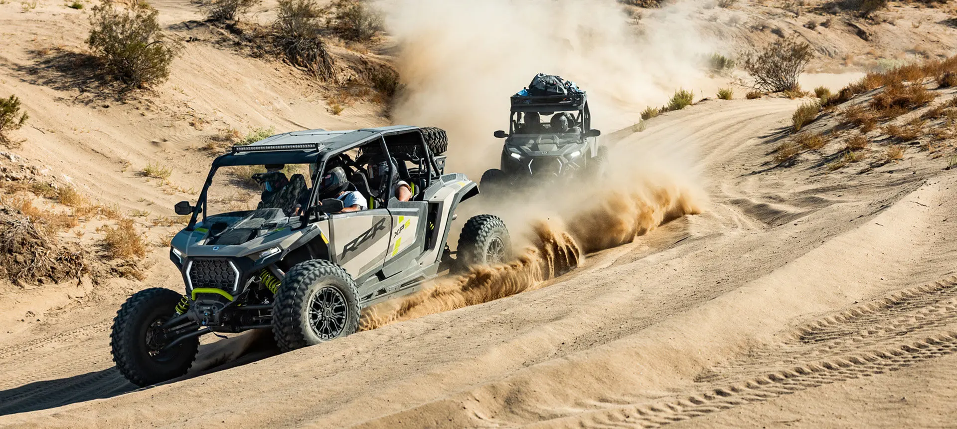 2 Polaris RZR XP side-by-sides driving in the desert with fully loaded cabs.