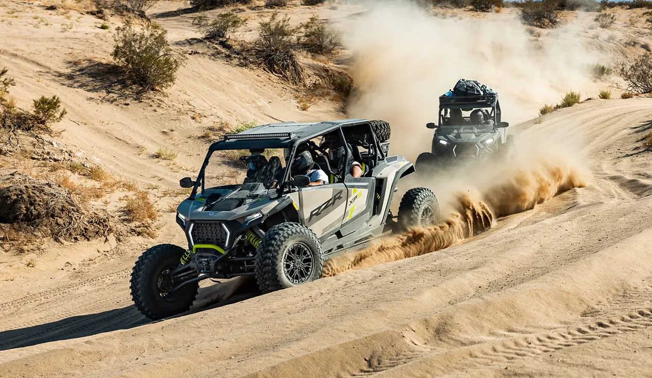 2 Polaris RZR XP side-by-sides driving in the desert with fully loaded cabs.