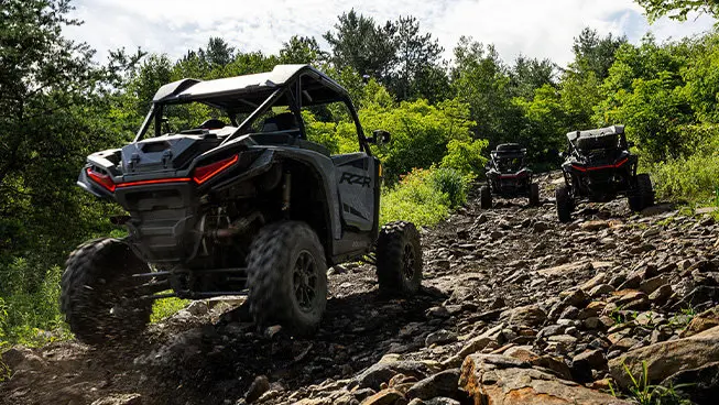 Three Polaris RZR XP side-by-sides driving on a rocky trail.