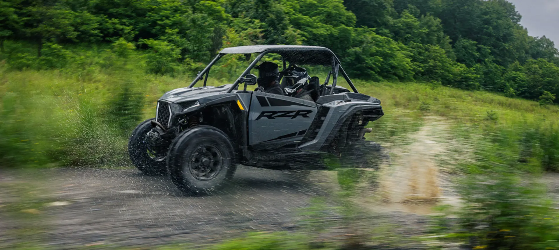 Side profile of a RZR XP side-by-side cruising down a forest trail.