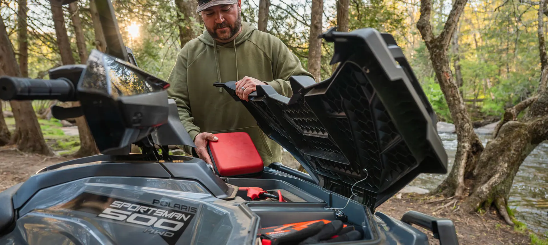 A man opening the the front cargo area on a Polaris Sportsman 500 ATV.
