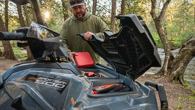 A man opening the the front cargo area on a Polaris Sportsman 500 ATV.