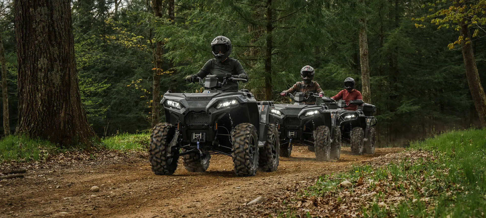 Three Polaris Sportsman 500 ATVs driving on a trail through the forest.