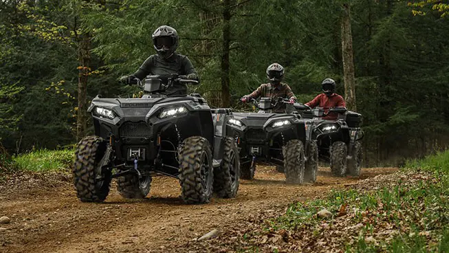 Three Polaris Sportsman 500 ATVs driving on a trail through the forest.