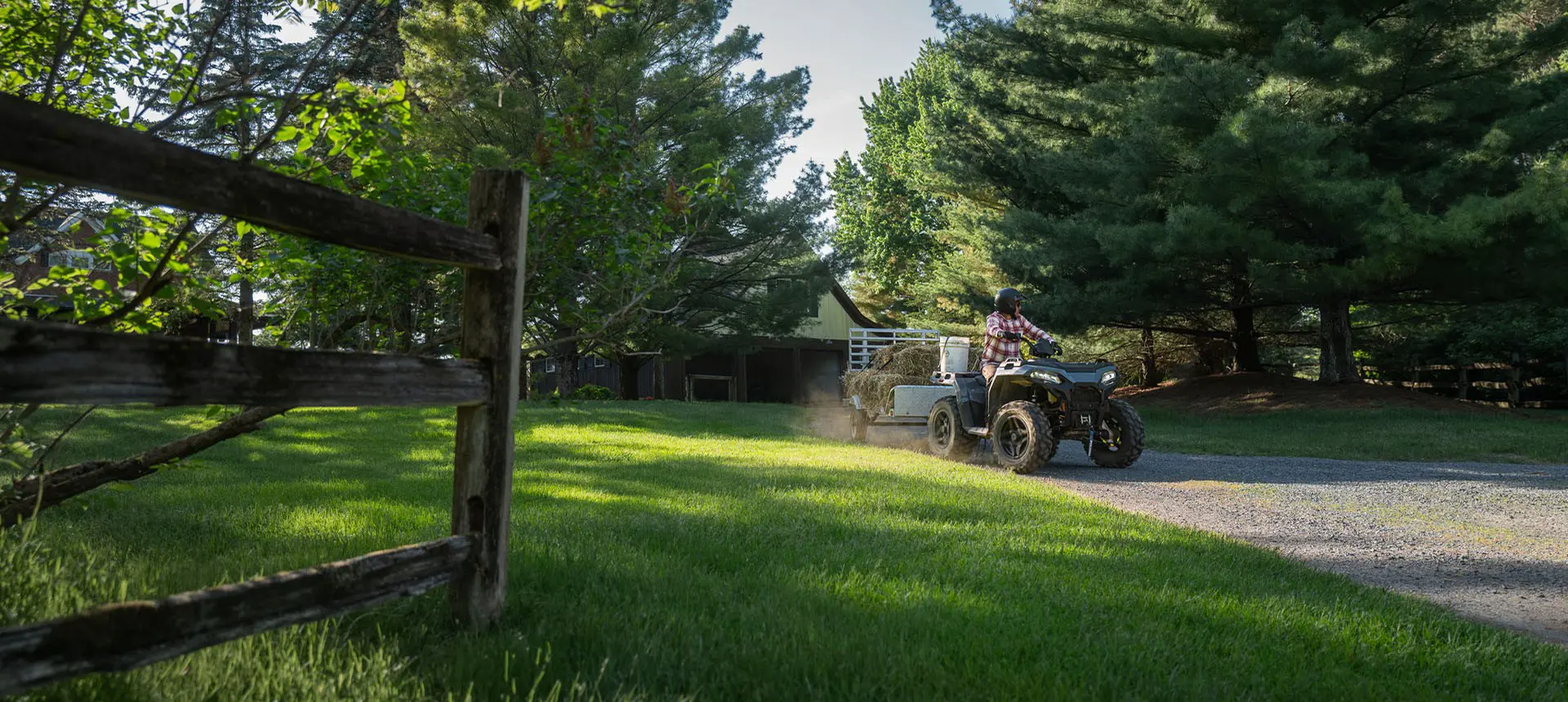 A rider on a Polaris Sportsman 500 ATV pulling a trailer loaded with hay bales.