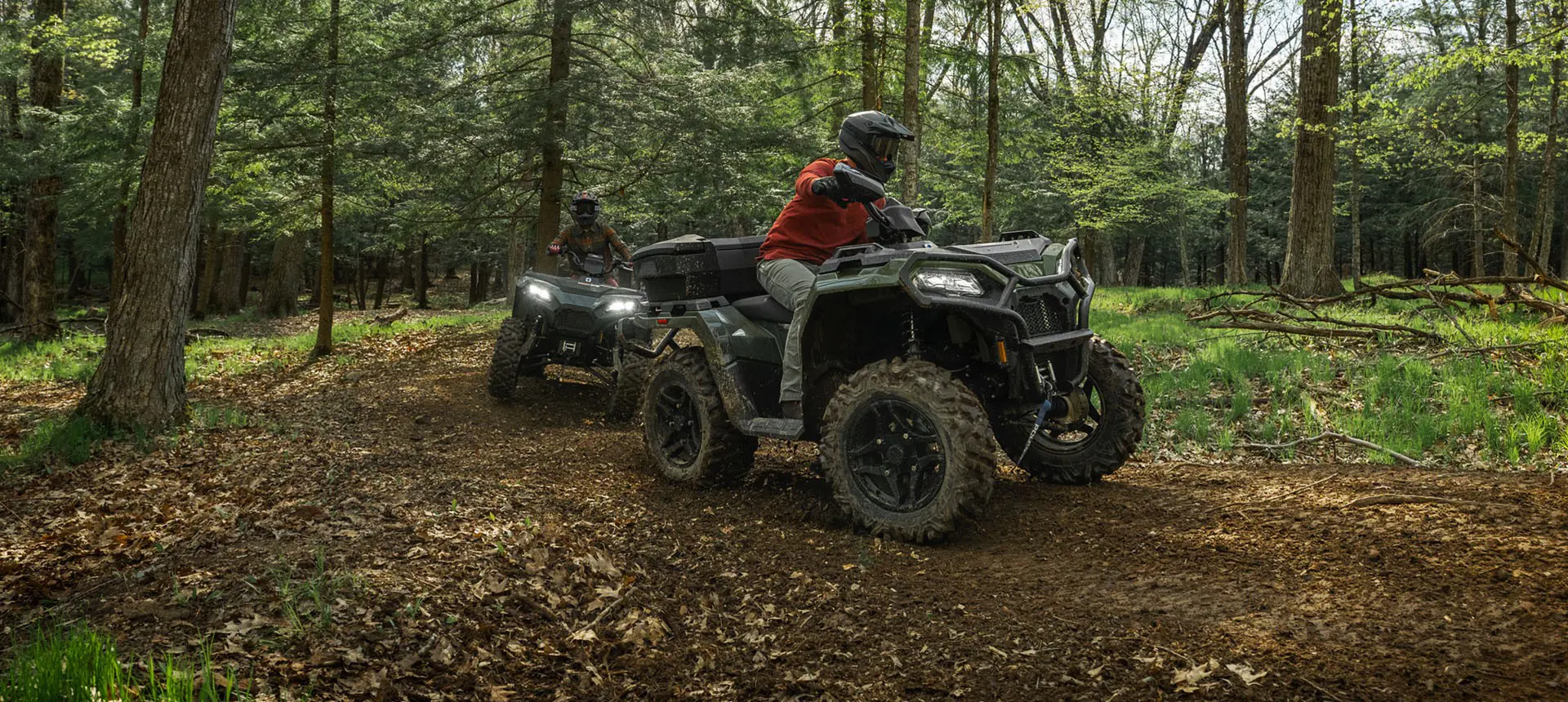 2 Polaris Sportsman 500 ATVs driving on a trail in the forest.