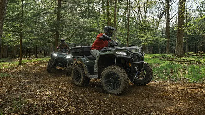 2 Polaris Sportsman 500 ATVs driving on a trail in the forest.