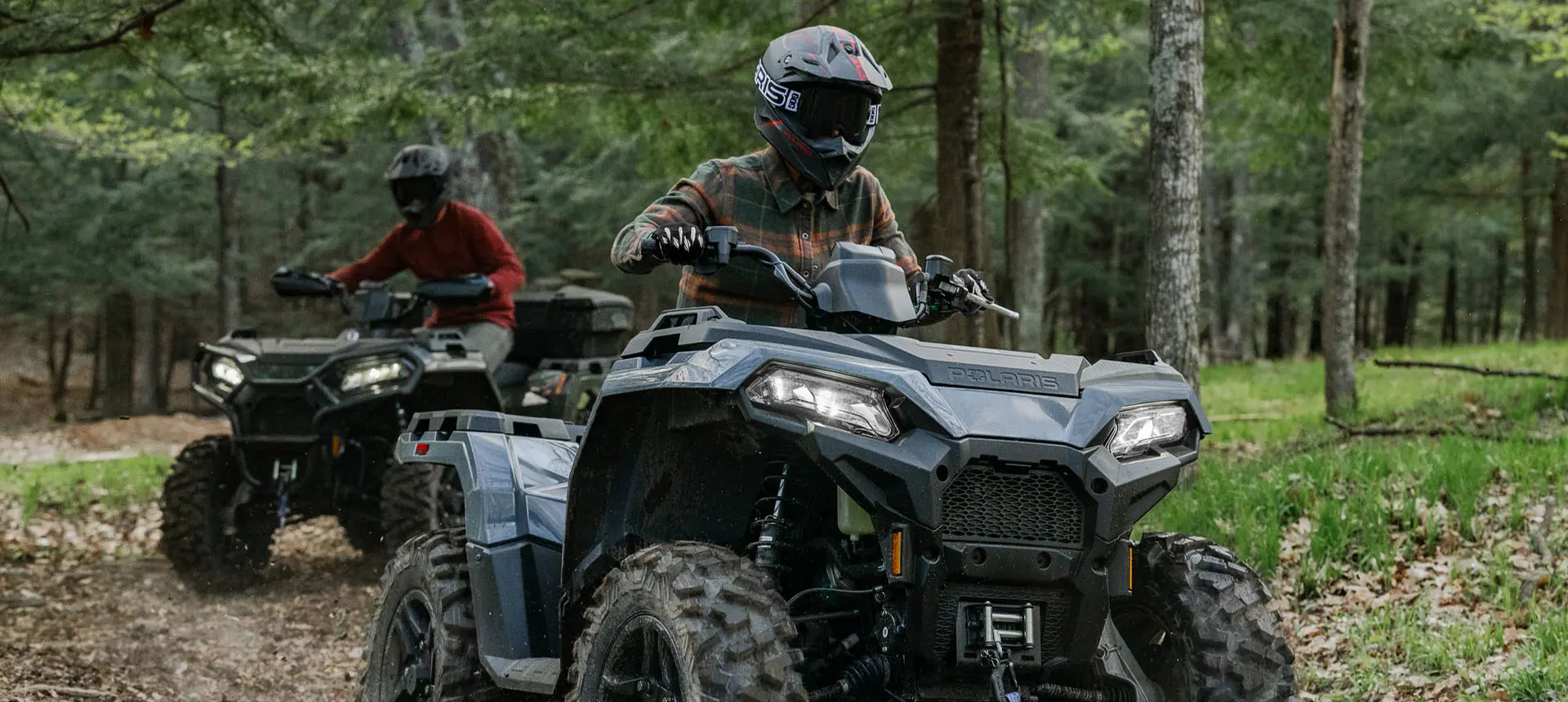 Rider on a Polaris Sportsman 500 ATV cruising on a trail with another Polaris ATV driving behind them.