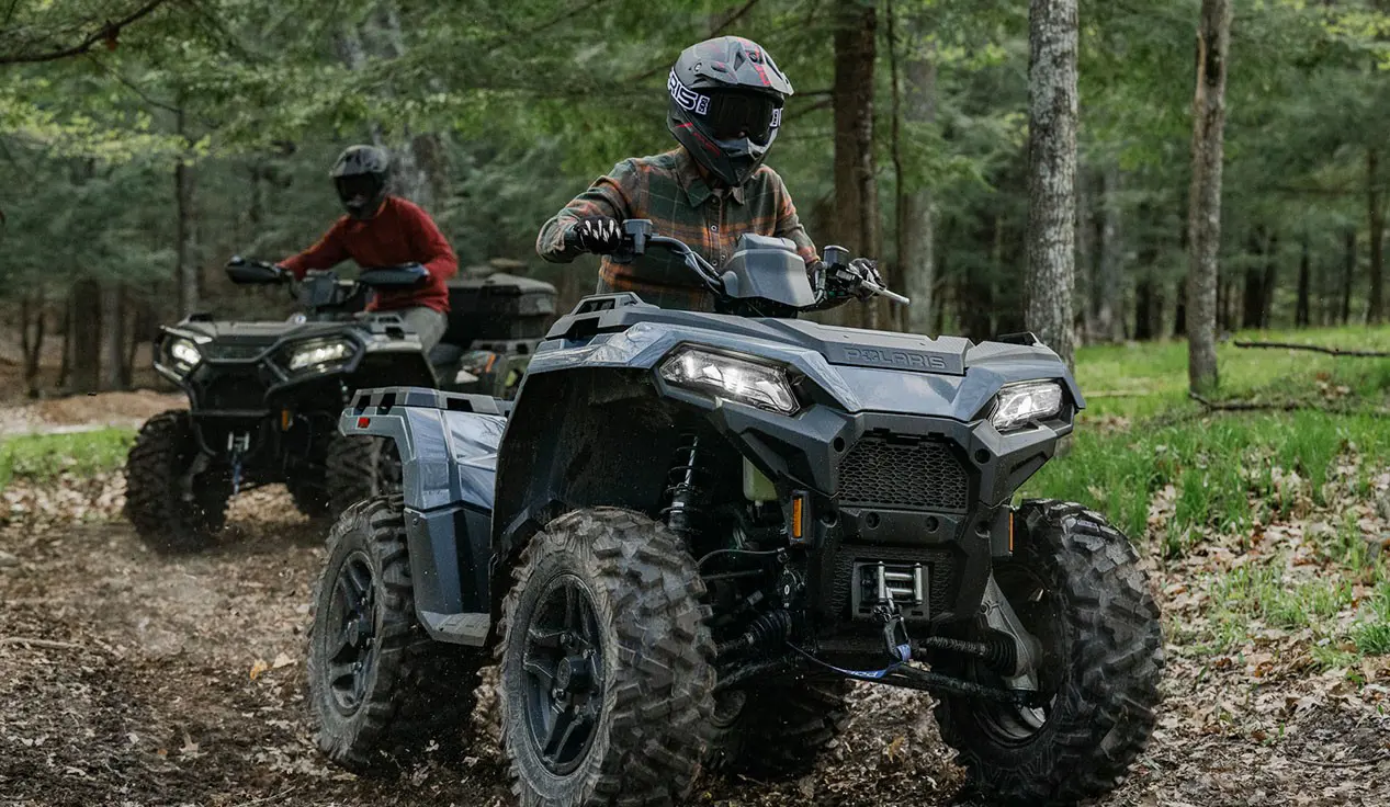 Rider on a Polaris Sportsman 500 ATV cruising on a trail with another Polaris ATV driving behind them.