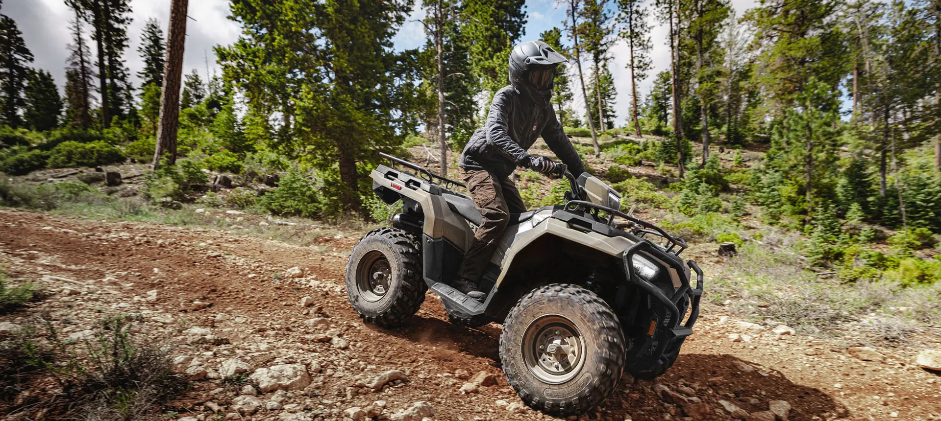 Rider on a Polaris Sportsman 600 ATV driving over uneven terrain in the forest.