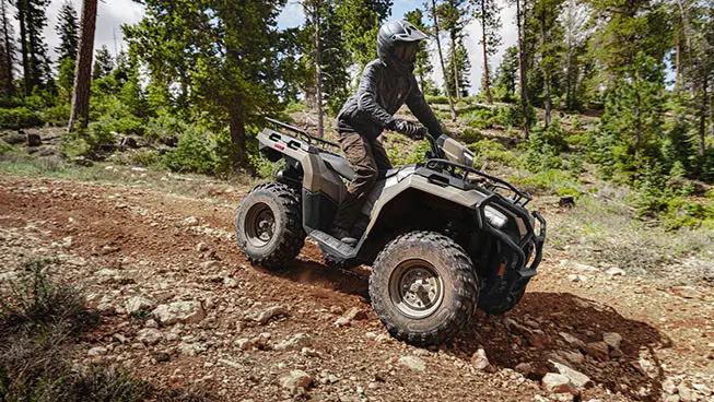 Rider on a Polaris Sportsman 600 ATV driving over uneven terrain in the forest.