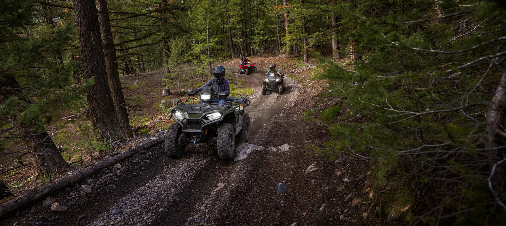 3 Polaris Sportsman ATVs driving on a forest trail.